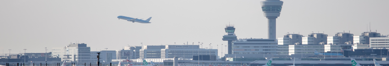 Een vliegtuig stijgt op vanaf luchthaven Schiphol met de verkeerstorens en terminalgebouwen op de achtergrond