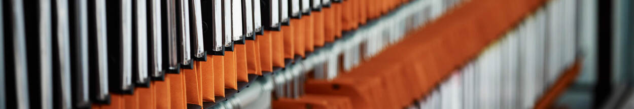 Close-up van een rij hangmappen in een archiefkast, met afwisselend zwarte en oranje tabbladen.